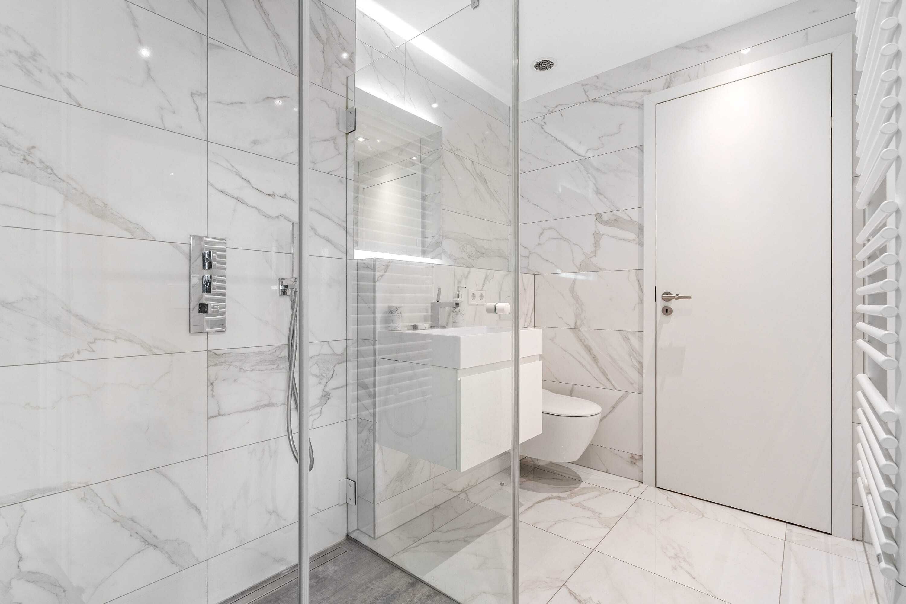 A modern bathroom with a glass-enclosed shower, a white toilet, and a marble-tiled floor.