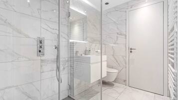 A modern bathroom with a glass-enclosed shower, a white toilet, and a marble-tiled floor.