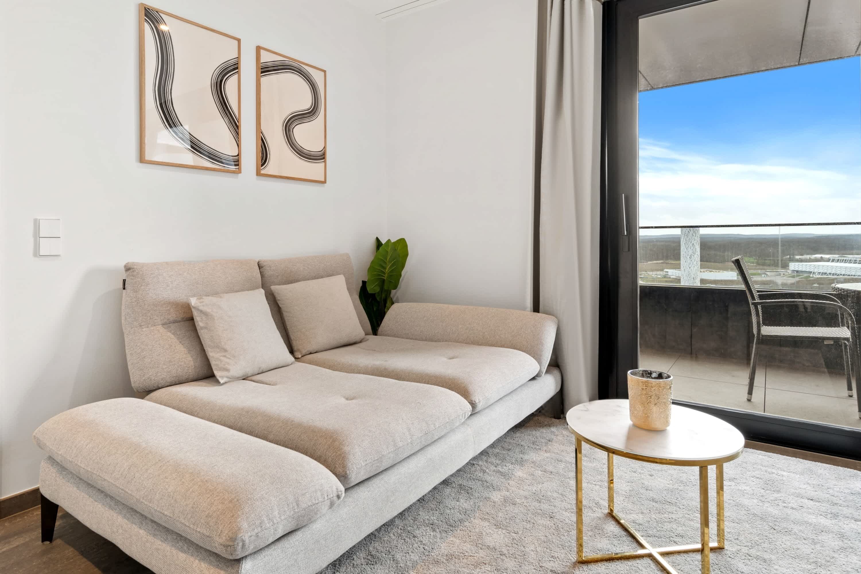 A modern living room with a beige sofa, a small round table, and two abstract paintings on the wall.