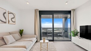 Un salon moderne comprenant un canapé, une petite table ronde, un téléviseur et une porte-fenêtre coulissante donnant sur un espace extérieur.