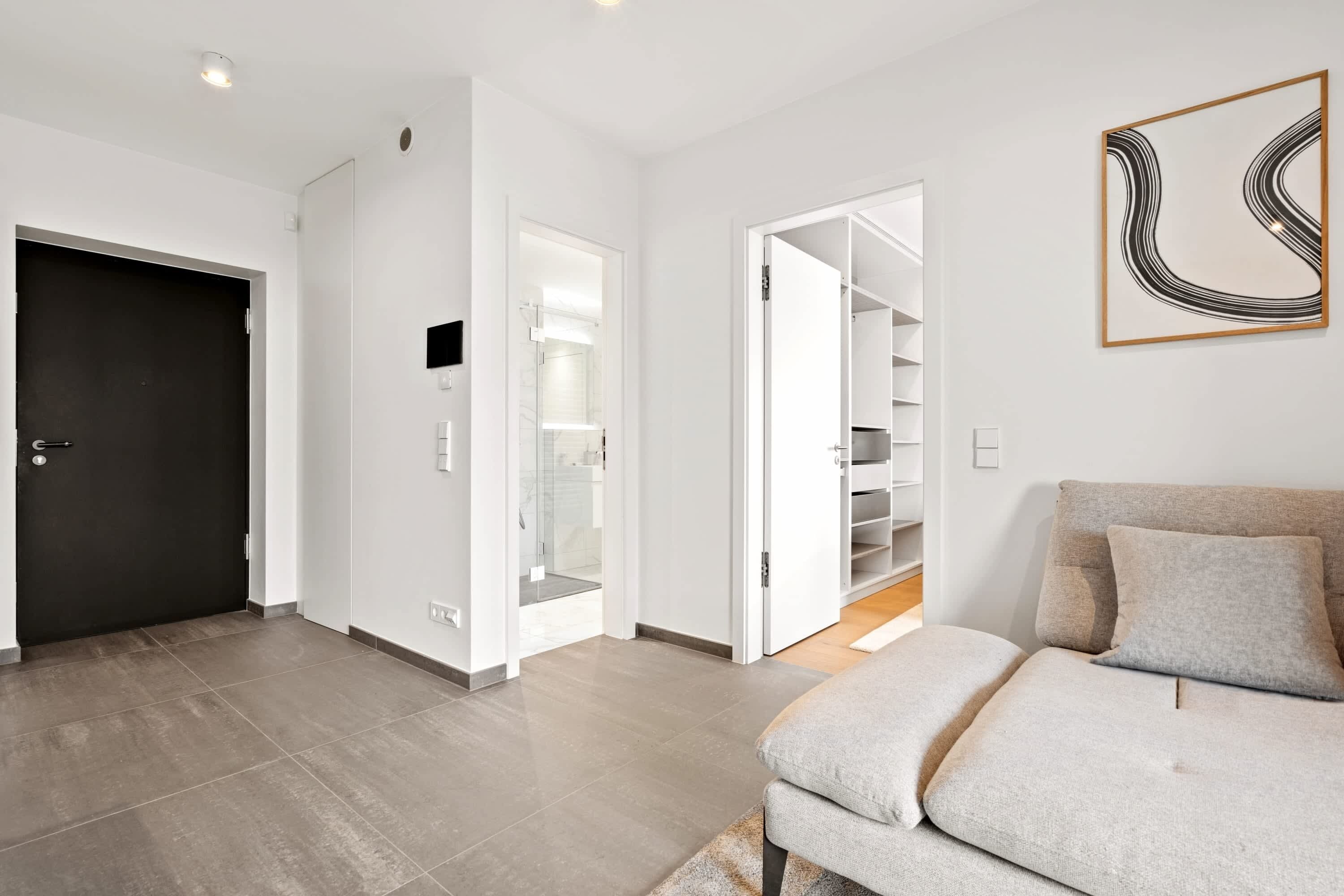 A modern living room with a sofa, a door, and a hallway leading to a closet.