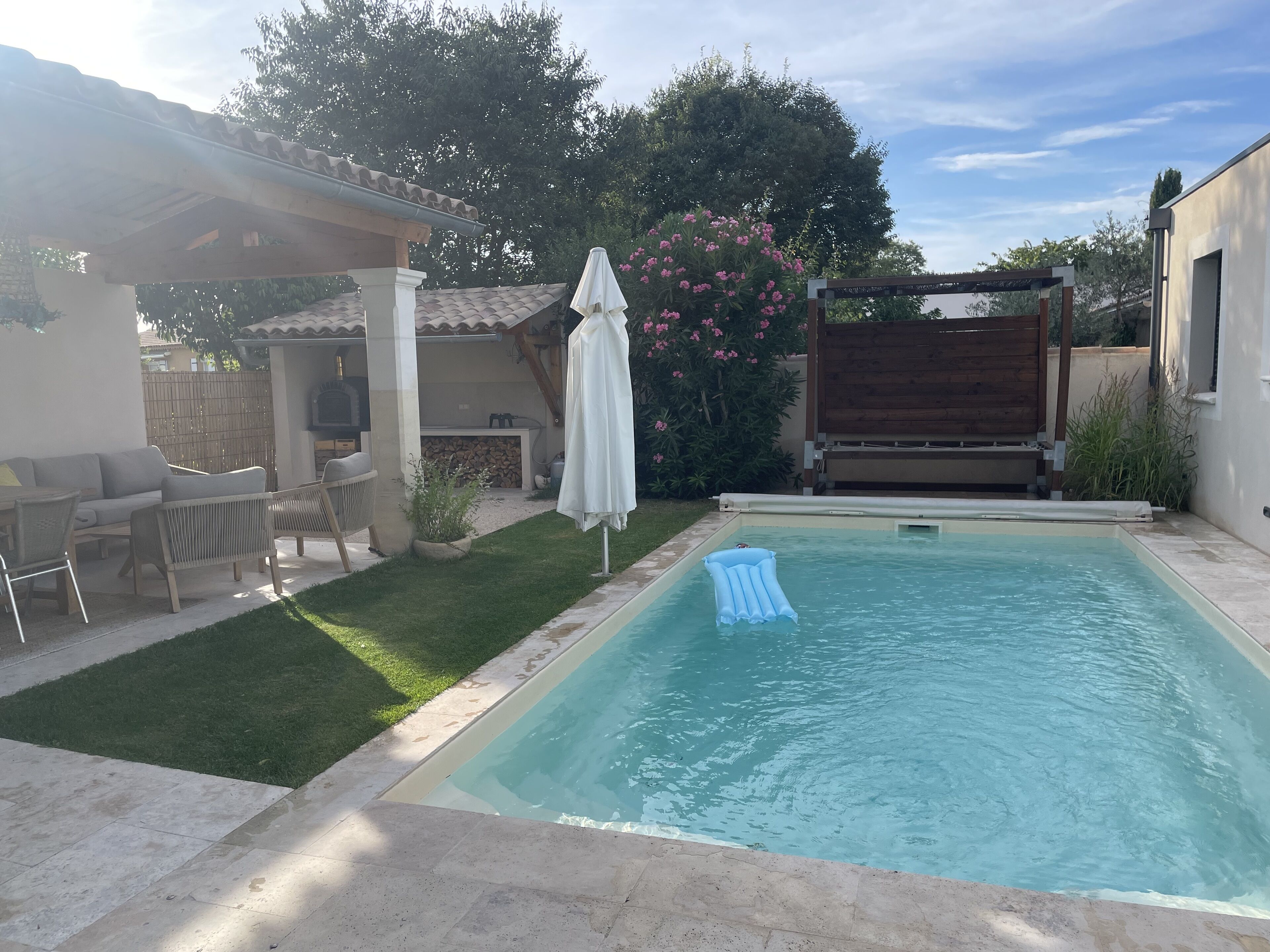 A swimming pool with a lounge area, a pergola, and a covered patio.