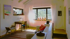 Een ruime kamer met een hoge plafond, een groot raam met gordijnen, een houten vloer en een witte bank.