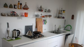 Een moderne keuken met witte kastjes, een gasfornuis, een waterkoker en diverse keukengerei.