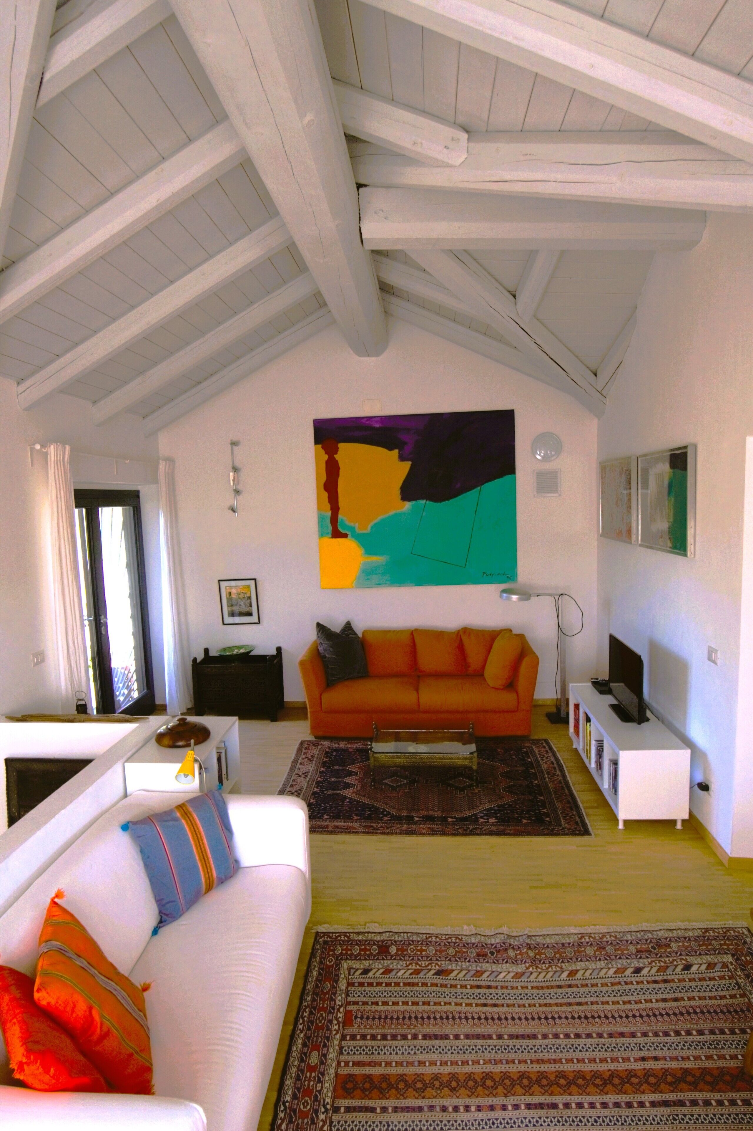 A living room with a white sofa, orange couch, and a colorful abstract painting on the wall.