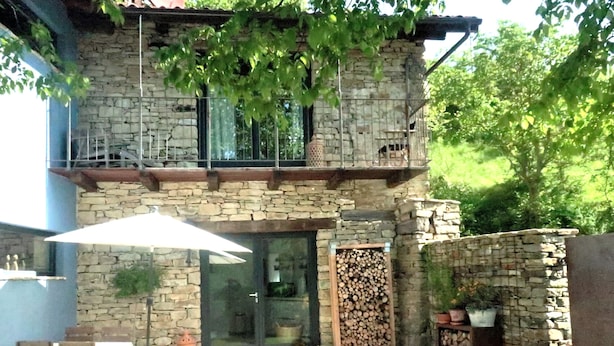 Een gebouw van steen met een balkon, een glazen deur en een patio met een tafel en stoelen.