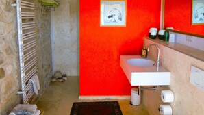 Een badkamer met een stenen muur, een rode accentmuur, een witte wastafel, een toilet en een zwart tapijt met een patroon.