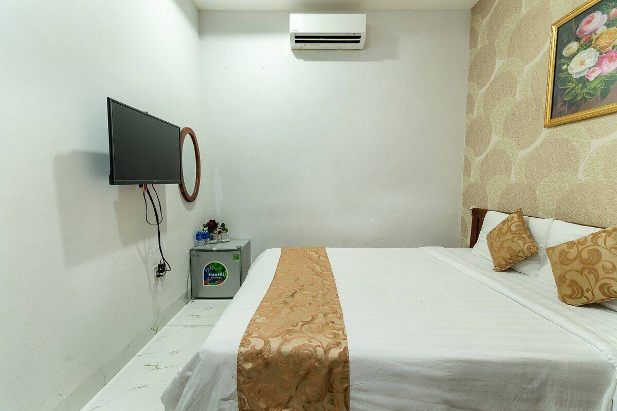 A hotel room with a bed, a television mounted on the wall, an air conditioner, and a small table with a decorative item.