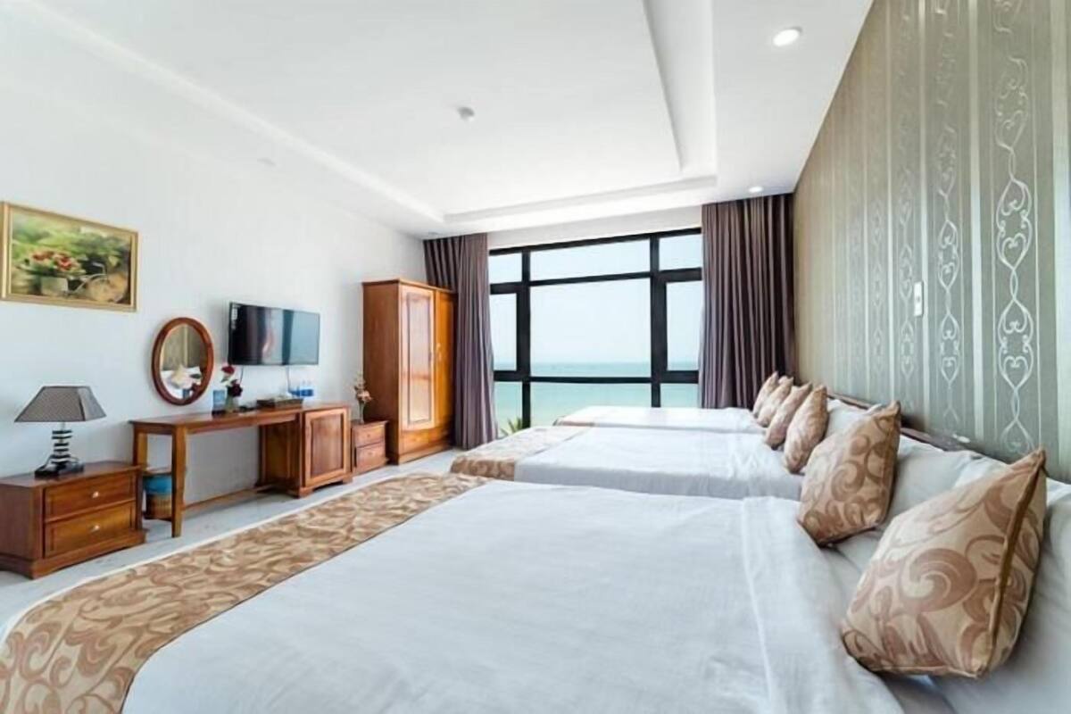 A hotel room with two beds, a desk, a TV, and a large window with a view.