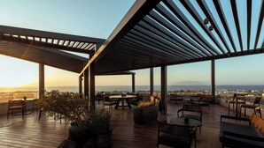 Eine Dachterrasse mit Holzboden, Sitzgelegenheiten im Freien und Blick auf die Stadtlandschaft.