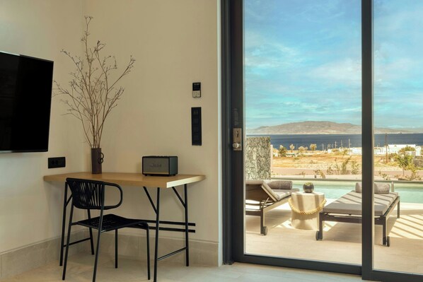Habitación moderna con zona de comedor, televisor de pantalla plana, un jarrón con ramas y vistas a una piscina y al paisaje.