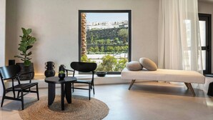 Ein modernes Wohnzimmer mit großem Fenster, einer Couch, einem Esstisch mit Stühlen und einem Blumentopf.