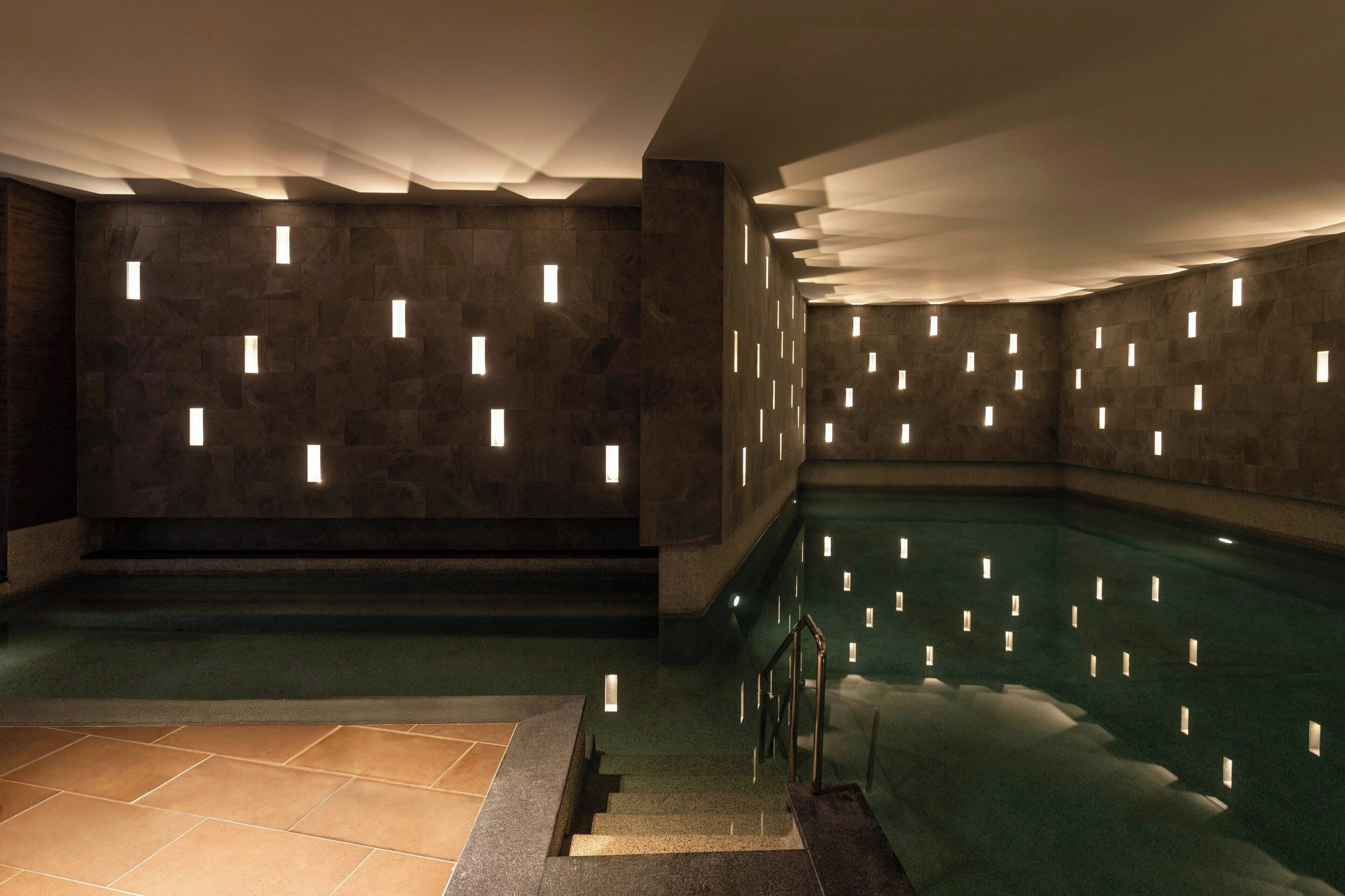 Un espacio de spa con piscina, paredes de piedra e iluminación empotrada.