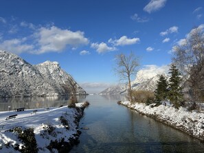 A snow-covered landscape with a calm river, benches, and mountains in the background. - Appartement Bergmann - Gemütliches Appartement am Traunsee mit Terrasse (Ebensee)