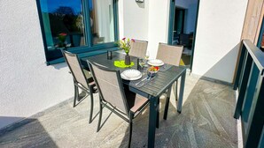 Un área de comedor al aire libre con una mesa y sillas, un florero con flores y vistas a las montañas a través de la ventana.