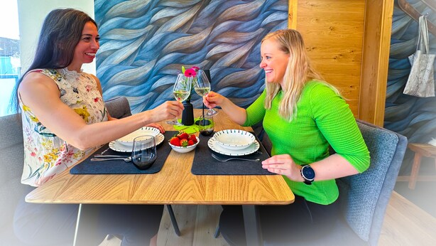Un comedor con una pared moderna de diseño ondulado, muebles de madera y una mesa dispuesta con platos, vasos y un bol de fresas.