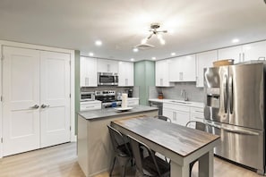 Una cocina moderna con armarios blancos, electrodomésticos de acero inoxidable y una mesa de comedor de madera.
