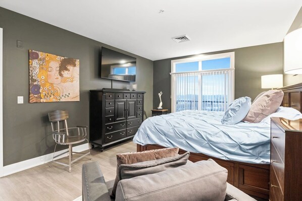 Une chambre à coucher comprenant un lit, une commode, une chaise, un téléviseur et une fenêtre donnant sur un beau paysage.