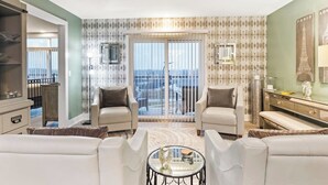 A spacious living room with two armchairs, a sofa, a coffee table, and a view of the city through large windows.