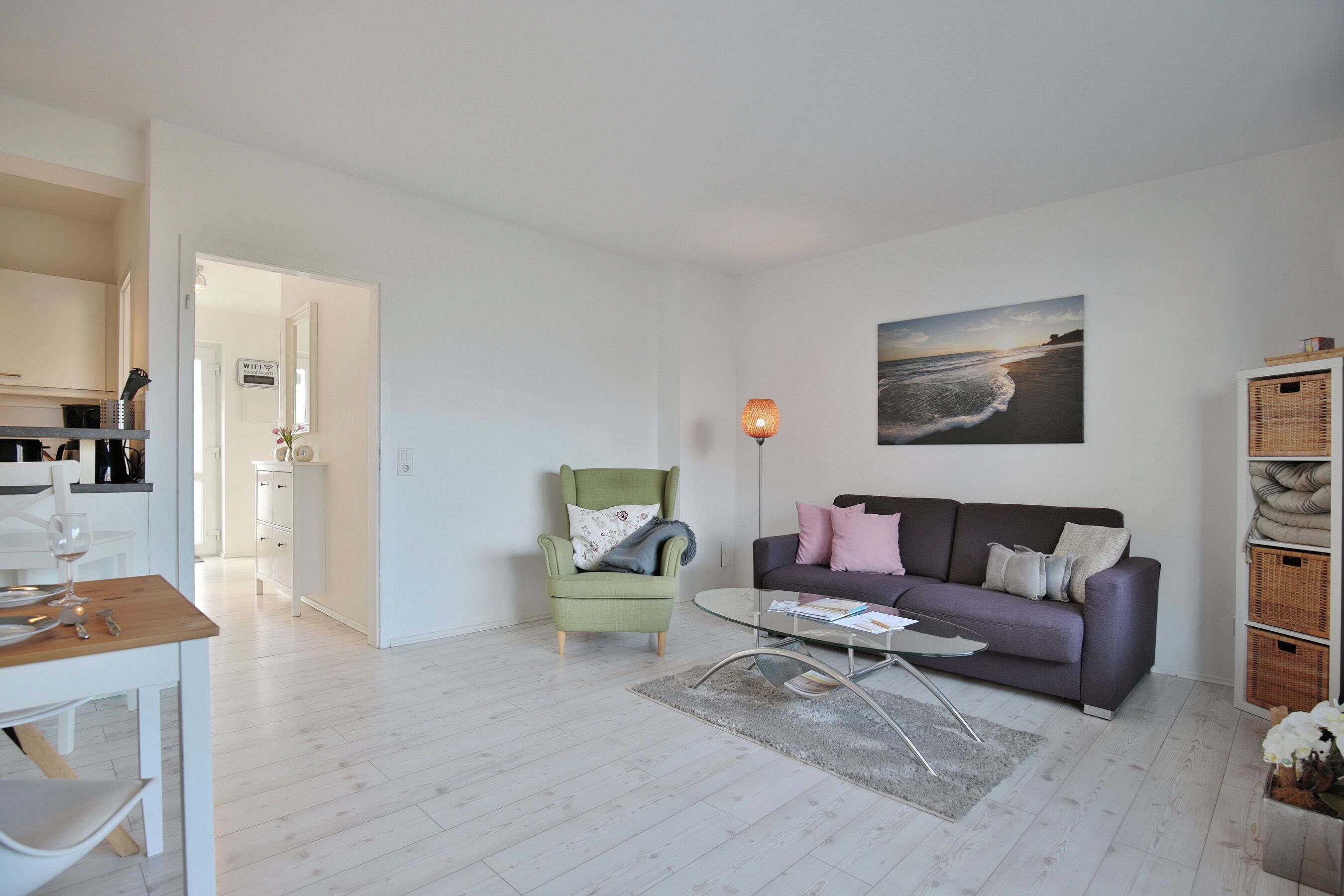 A modern living room with a sofa, armchair, coffee table, and a painting of a beach scene.