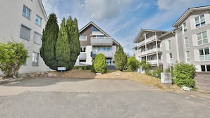Un immeuble résidentiel doté de nombreux balcons, d’une allée pavée et entouré de verdure.