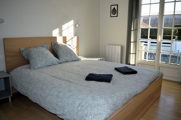 A bedroom with a large bed, two pillows, a nightstand, a radiator, and a window with a view of buildings.