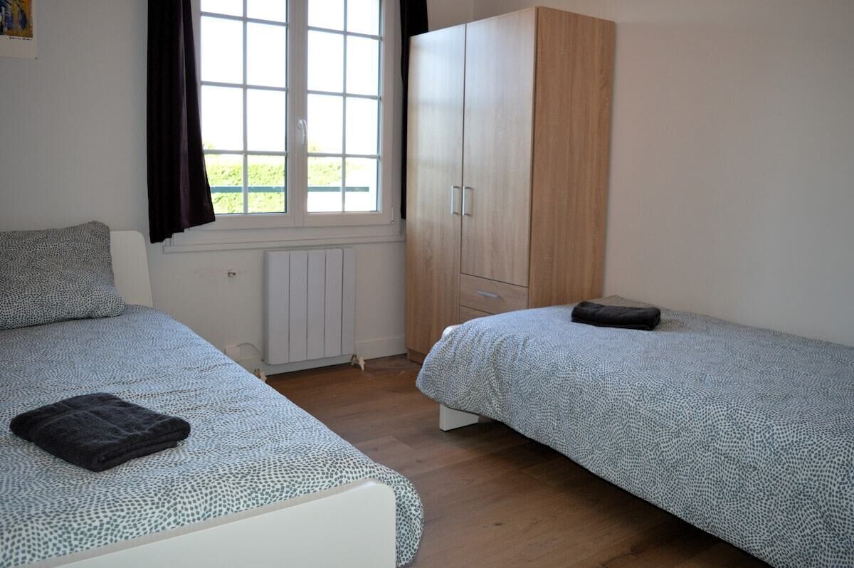 Quarto com duas camas, um guarda-roupa e janela com cortinas.