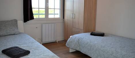 Quarto com duas camas, um guarda-roupa e janela com cortinas.