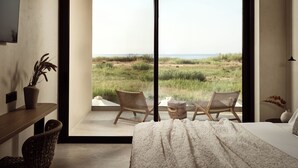 A bedroom with a large sliding glass door leading to a balcony with two wicker chairs and a view of the beach. - Mayamor Villas (Zakynthos)