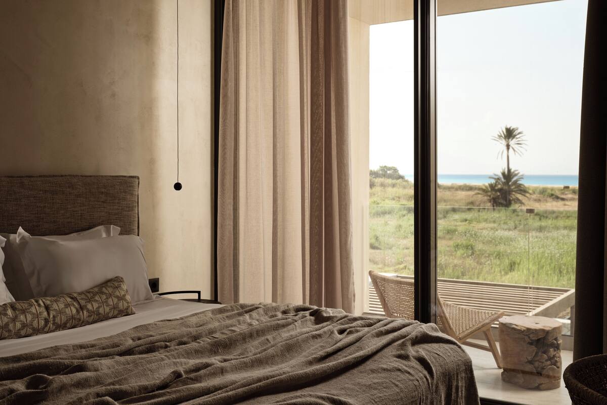 Un dormitorio con una cama grande, vistas a la playa y un balcón con una silla.