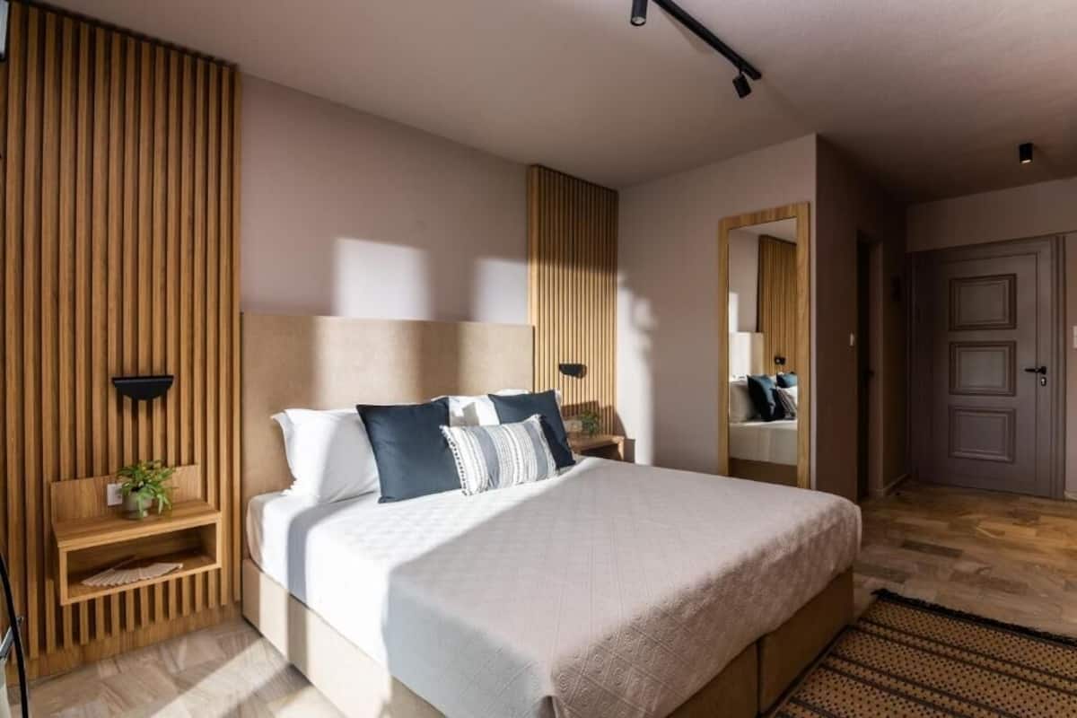 A modern bedroom with a large bed, wooden paneling, a bedside table with a plant, and a mirror.