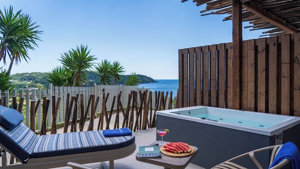Eine Holzterrasse mit Whirlpool, Liegestühlen und einem Tisch mit Getränk und Wassermelone.
