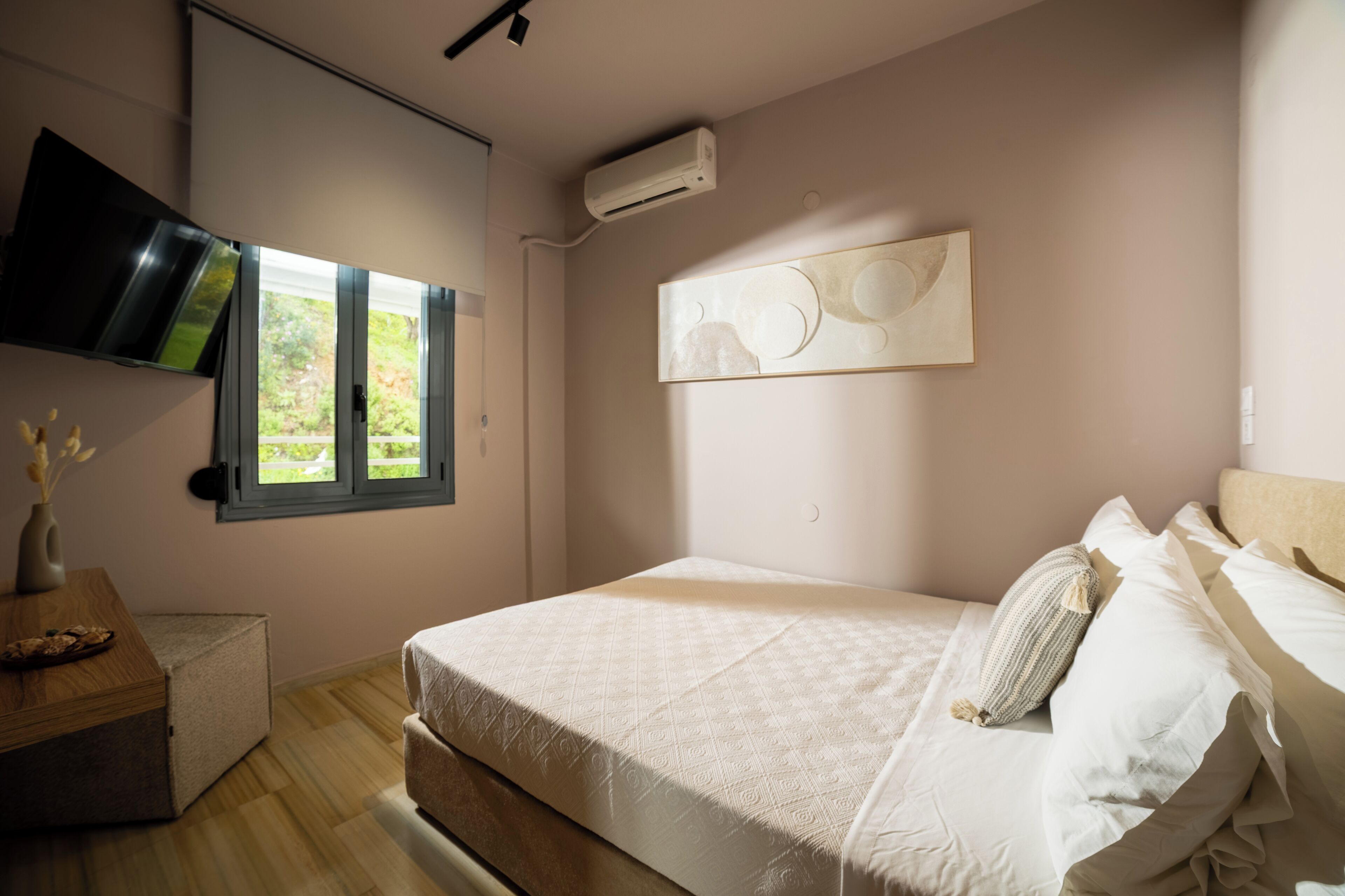 A bedroom with a bed, a window, a wall-mounted air conditioner, and a painting.