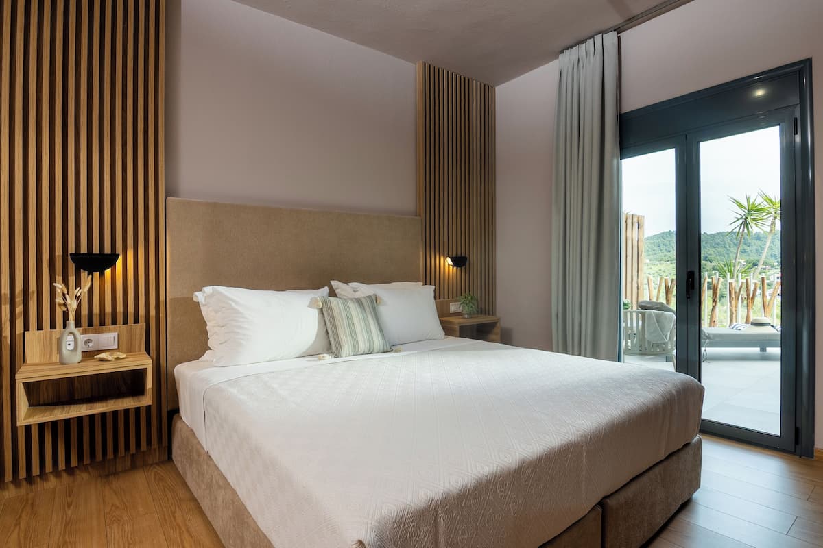 A modern bedroom with a large bed, wooden paneling, a nightstand with a lamp, and a view of a balcony.