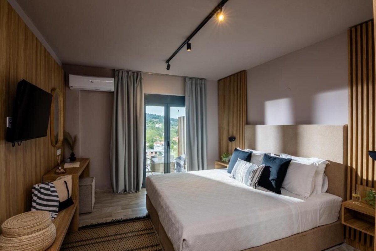 Une chambre d’hôtel moderne dotée d’un grand lit, d’un téléviseur à écran plat, d’une table de chevet en bois, d’un petit coin salon et offrant une vue à travers la porte vitrée.