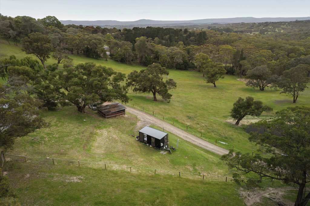 Una finca rural amb un camp tancat per una valla, una cabana de fusta i un camí rural.