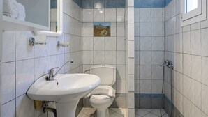 Une salle de bain avec un lavabo, des toilettes et une douche, le tout de couleur blanche.