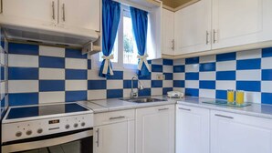 Une cuisine compacte avec des meubles blancs, un crédence à carreaux bleus et blancs, un four encastré et un évier.