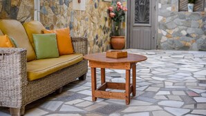 Un canapé en osier avec des coussins, une petite table en bois et un mur de pierre agrémenté d’une porte et de plantes en pot.