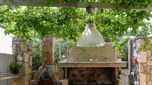 Un espace barbecue extérieur en pierre, agrémenté d’un luminaire suspendu, de murs en pierre et d’un banc en bois.