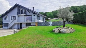 Una moderna casa a due piani con fondamenta in pietra, un prato curato e un piccolo albero.