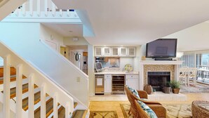A spacious living area with a fireplace, a television, and a dining area with chairs. - Views of Osprey Lake in Pelican Watch 4 Bedroom (Pawleys Island)