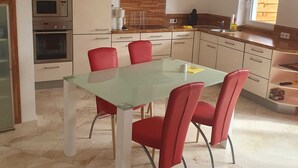 A modern kitchen with a dining area, featuring a glass table and red chairs, a built-in oven, and a window providing natural light. - Ruhige Ferienwohnung am Stadtrand von Lindau Inmitten von Wiesen und Obstbäumen (Lindau (Bodensee))