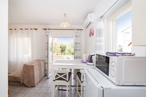 A compact kitchen with a dining area, a sofa, and a view through the window.