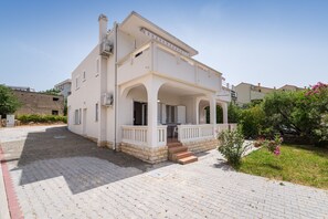 A two-story house with a covered porch, a paved driveway, and a garden with flowering plants.