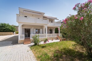 A two-story house with a covered porch, a stone wall, and a garden with pink flowers. - Cozy Apartment Marija With Garden (Novalja)