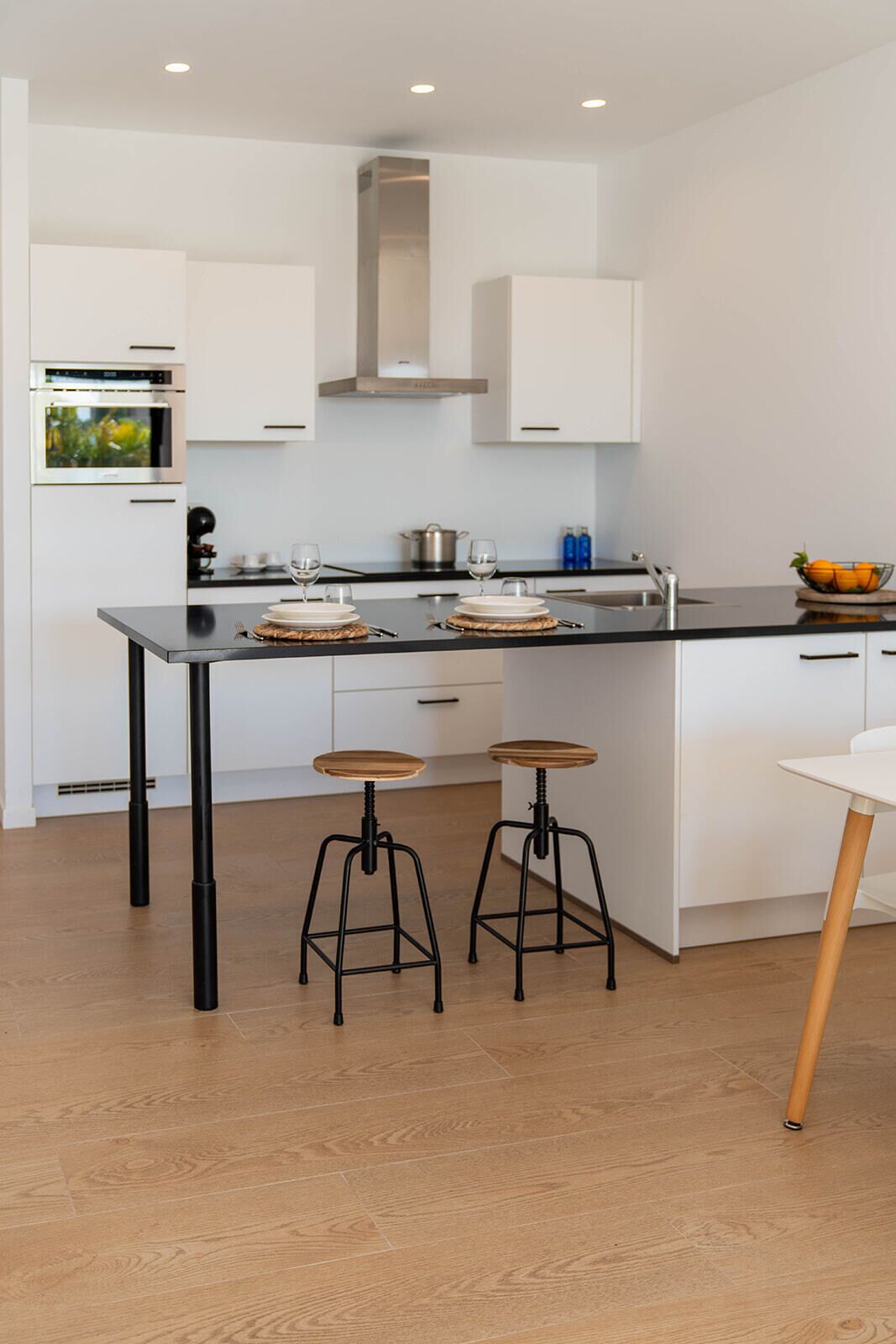 A modern kitchen with white cabinetry, a black countertop, and two stools.
