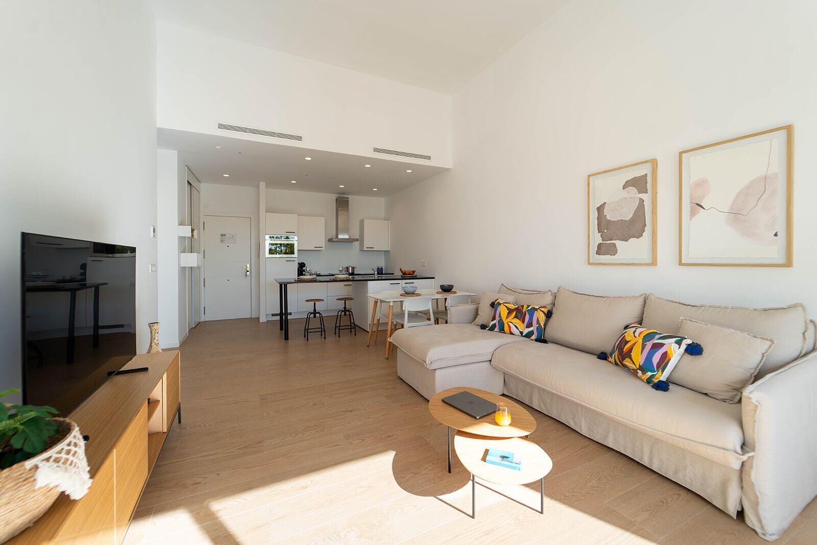 A modern living room with a sofa, coffee table, and a TV. There is a kitchen area with a dining table and chairs.