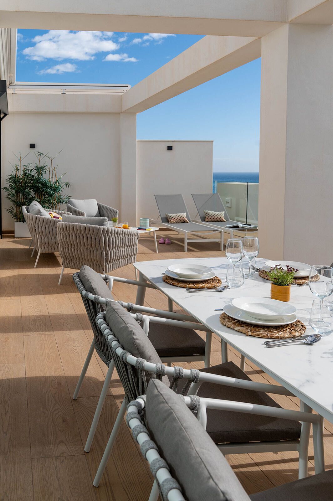 A rooftop terrace with a dining table set for four, surrounded by wicker chairs and a sofa.
