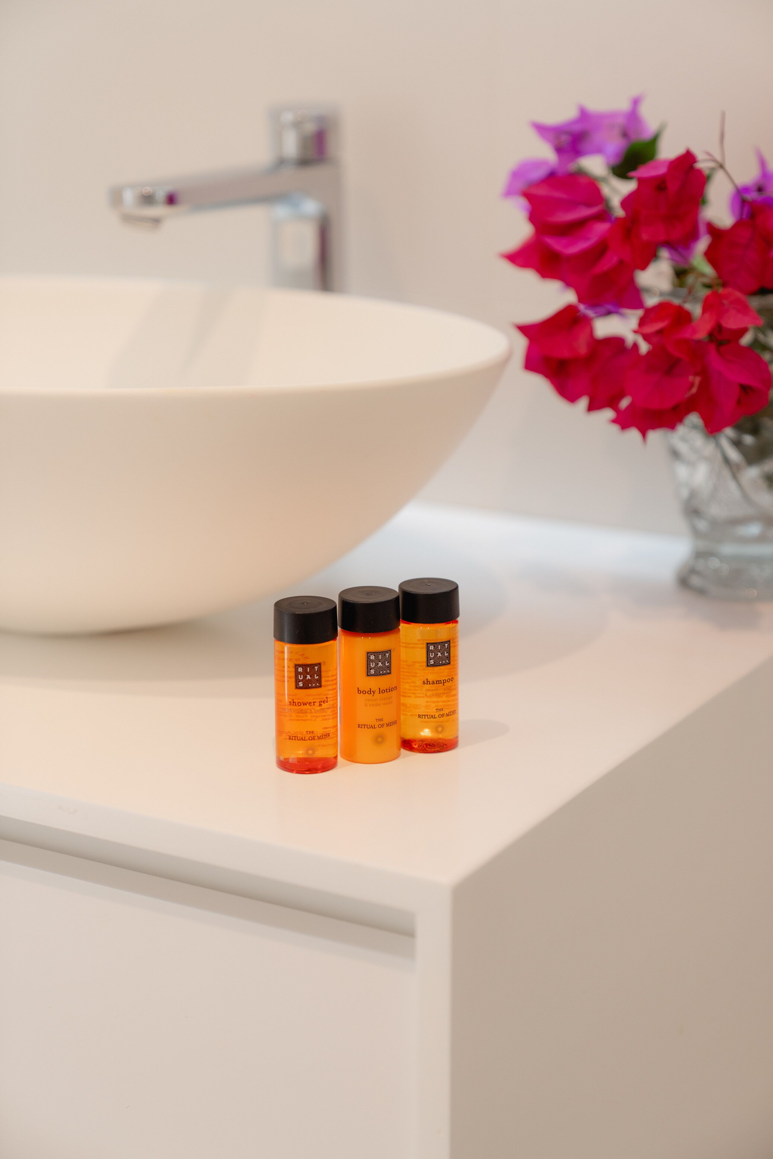 A bathroom with a white sink, a mirror, and three bottles of body lotion on the counter.